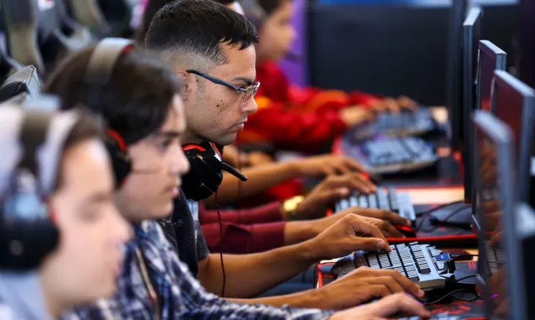 Grupo de jovens usando headsets e computadores em uma sala de treinamento tecnológico ou arena de jogos.